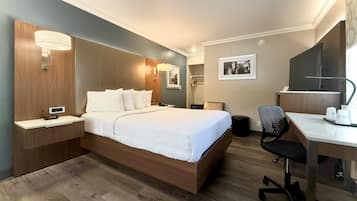 A hotel room with a bed, bedside table, desk, chair, and a mirror.