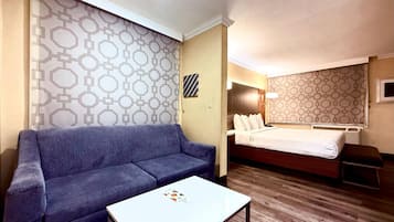 A hotel room with a sofa, a small table, a bed, and patterned wallpaper.