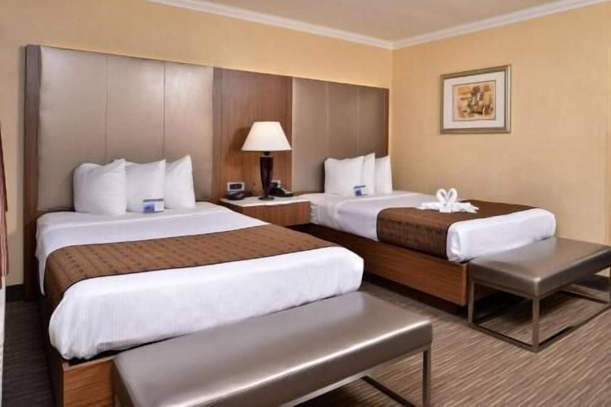 Ein Hotelzimmer mit zwei Betten, einer Bank, einem Nachttisch mit Lampe und einem gerahmten Bild an der Wand.