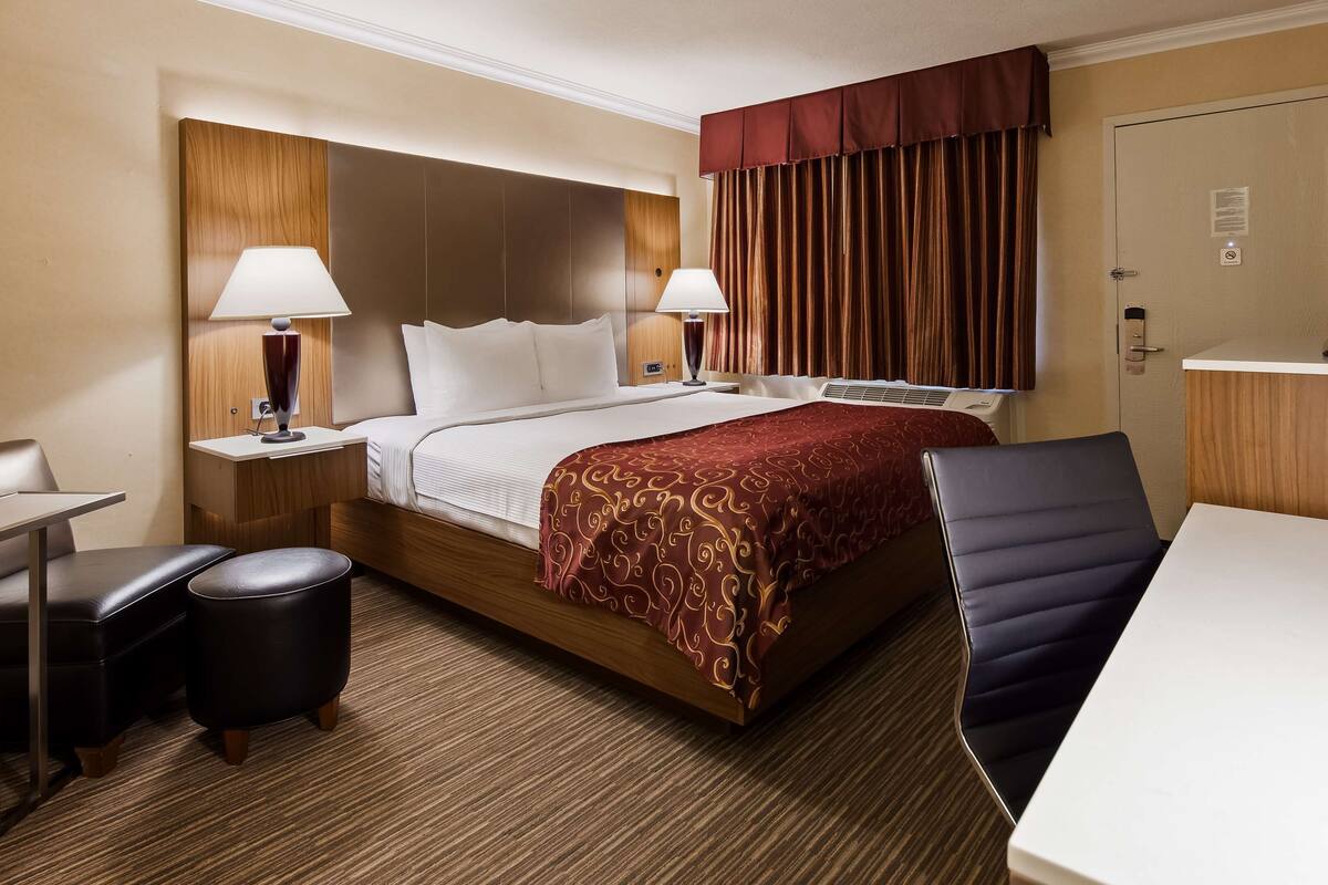 Ein Hotelzimmer mit einem Bett, zwei Nachttischen mit Lampen, einem Schreibtisch, einem Stuhl und einem Fernseher.