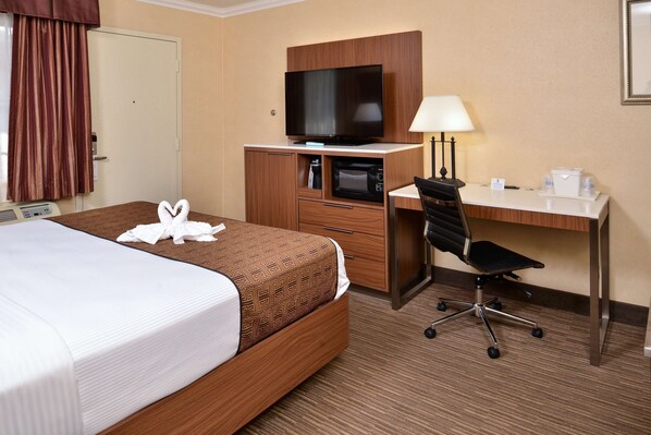 A hotel room with a bed, a desk with a computer, a television, a lamp, and a microwave.