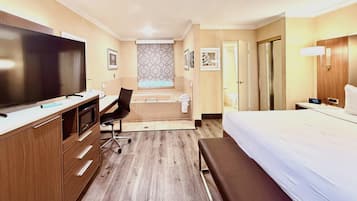 Habitación de hotel con cama, escritorio, silla, televisor y baño con ducha e inodoro.