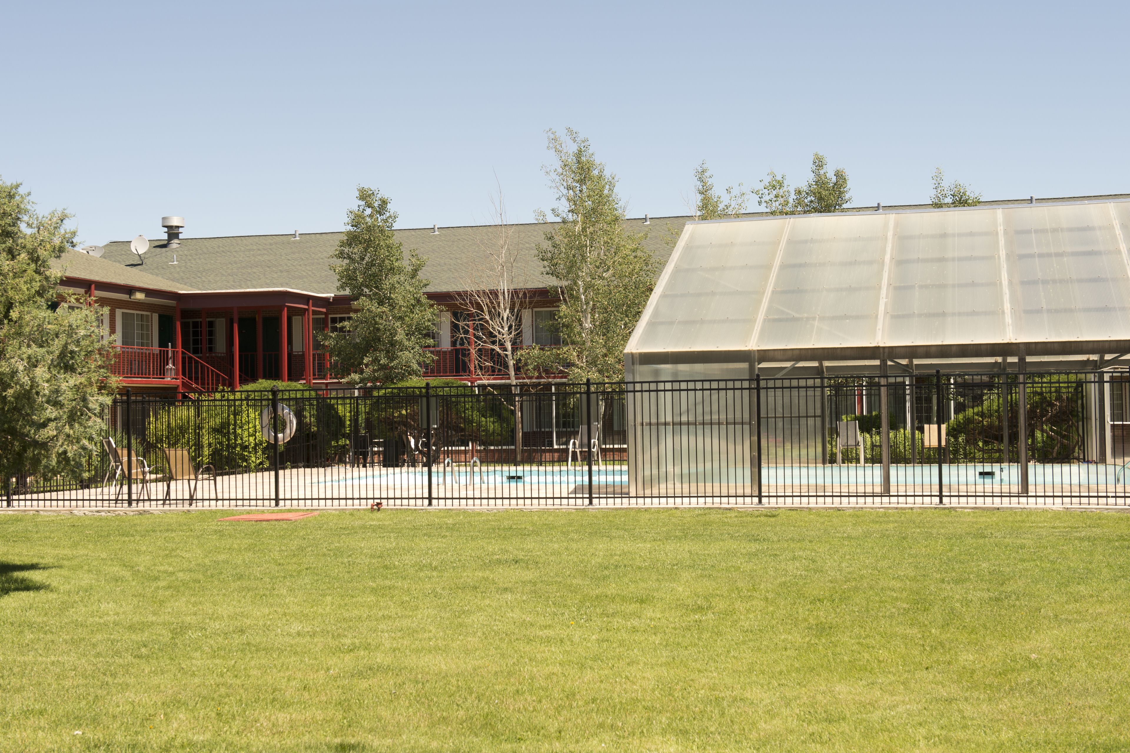 Una casa con piscina, patio cercado y una amplia estructura de invernadero de vidrio.