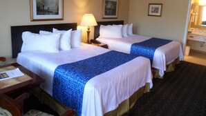 Habitación de hotel con dos camas, un escritorio, una silla, una lámpara y cuadros en las paredes.