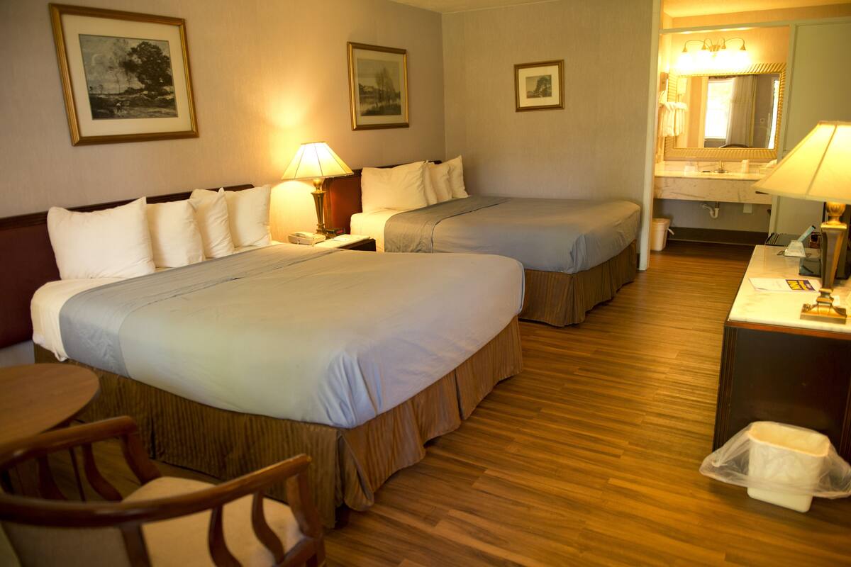 Une chambre d’hôtel avec deux lits, un bureau, une chaise, une salle de bain et des tableaux encadrés aux murs.