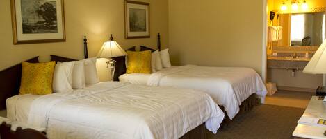 A hotel room with two beds, a desk, a mirror, and framed artwork on the walls.