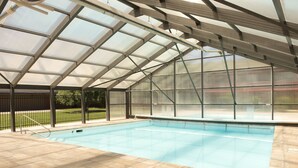 Una piscina interior con techo de cristal, rodeada de un suelo de baldosas.