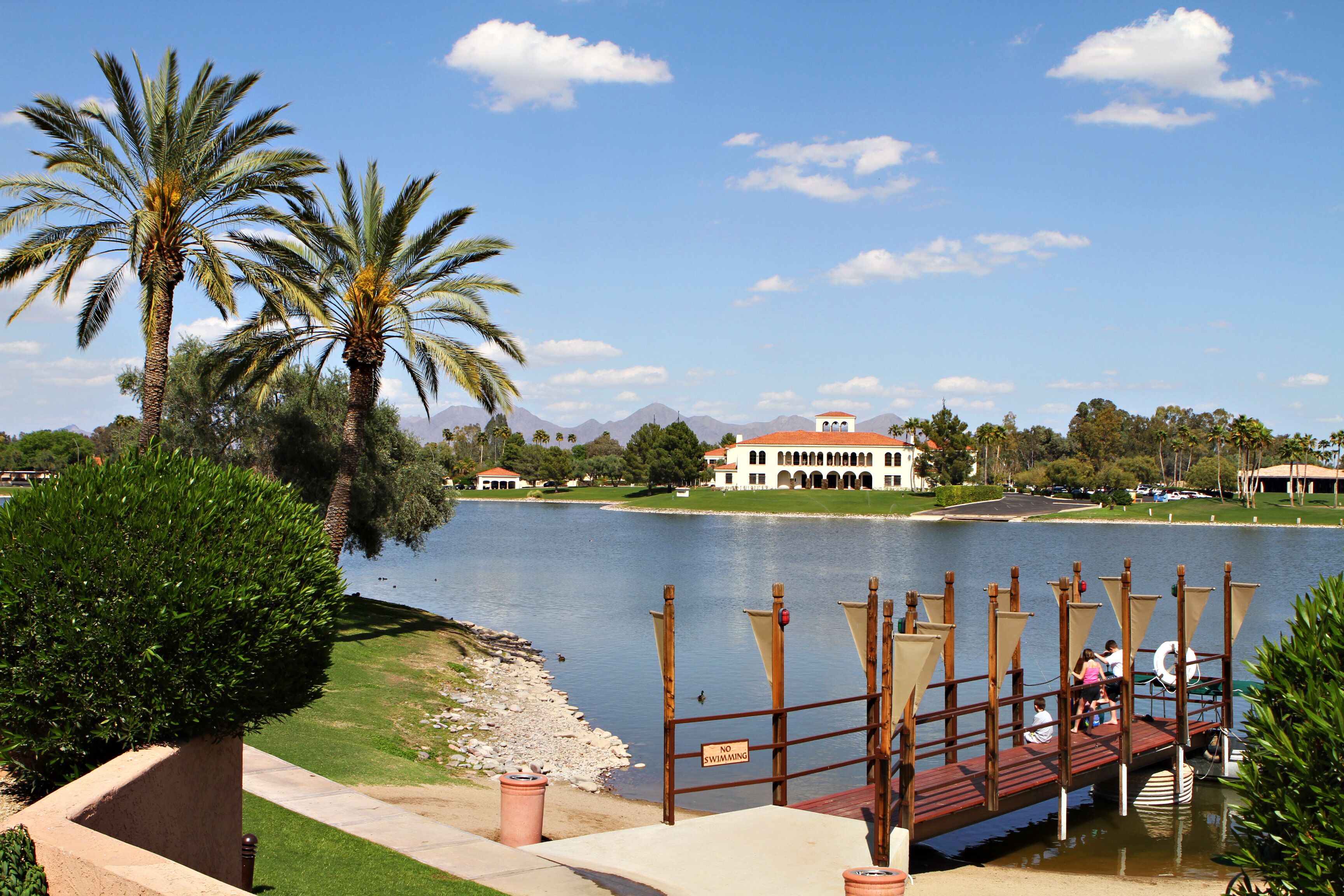 Vista de un lago con un muelle, palmeras y un edificio al fondo.
