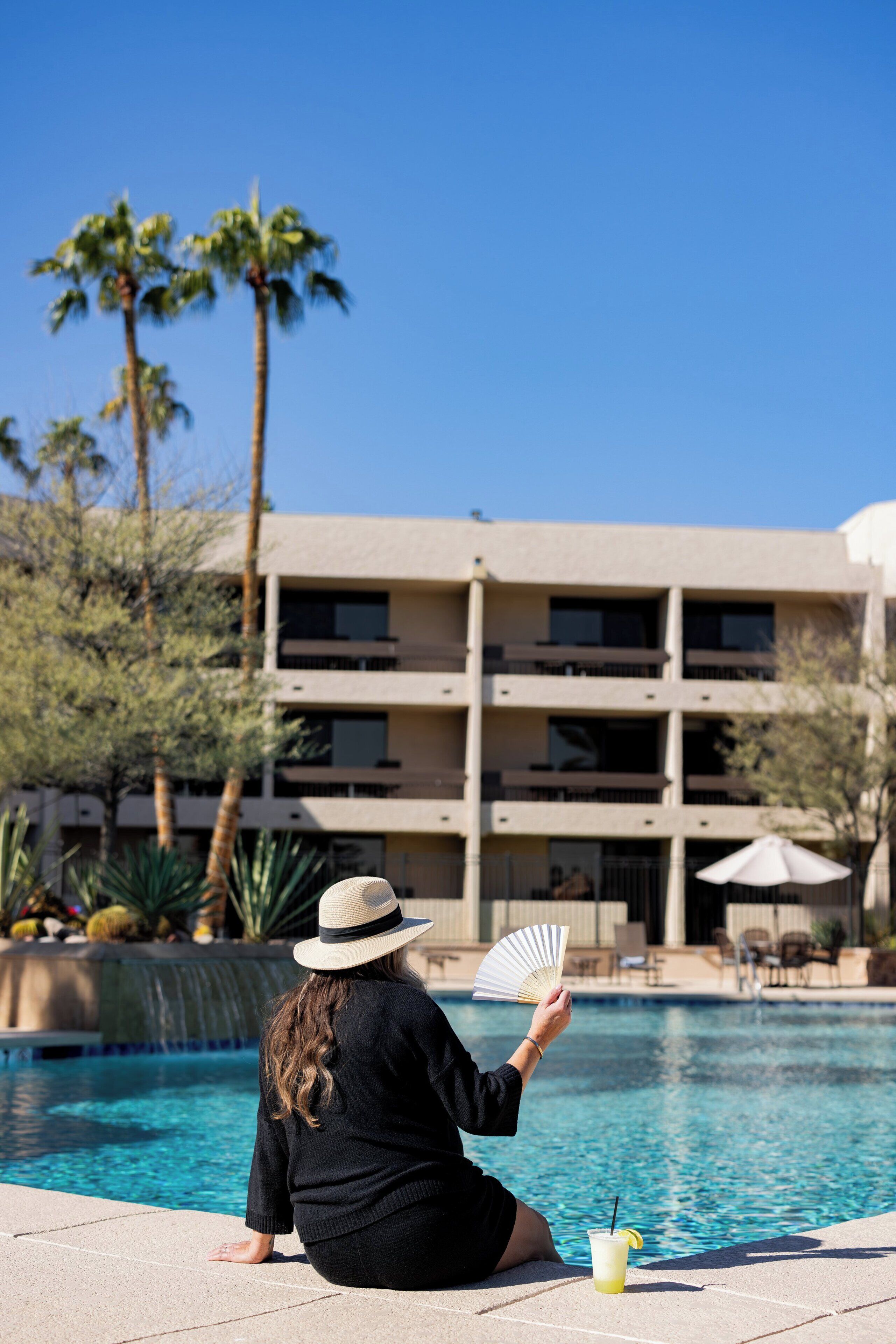 A person sitting by a pool with a building in the background.