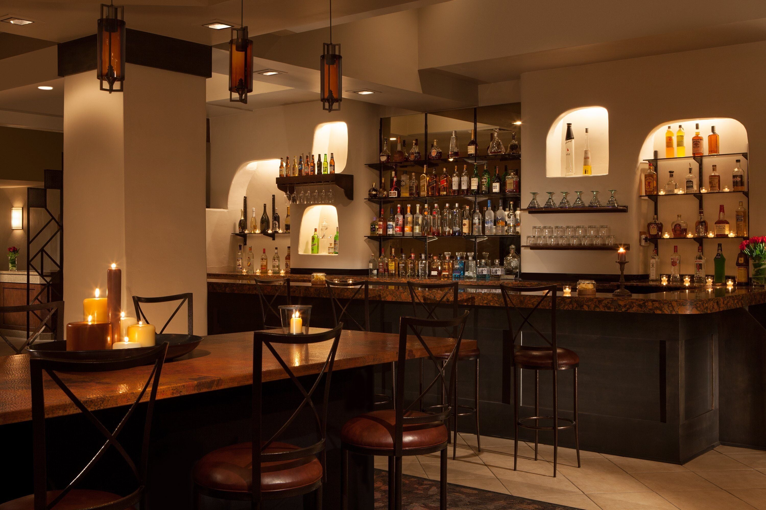 A bar area with a wooden counter, multiple shelves of bottles, and bar stools.