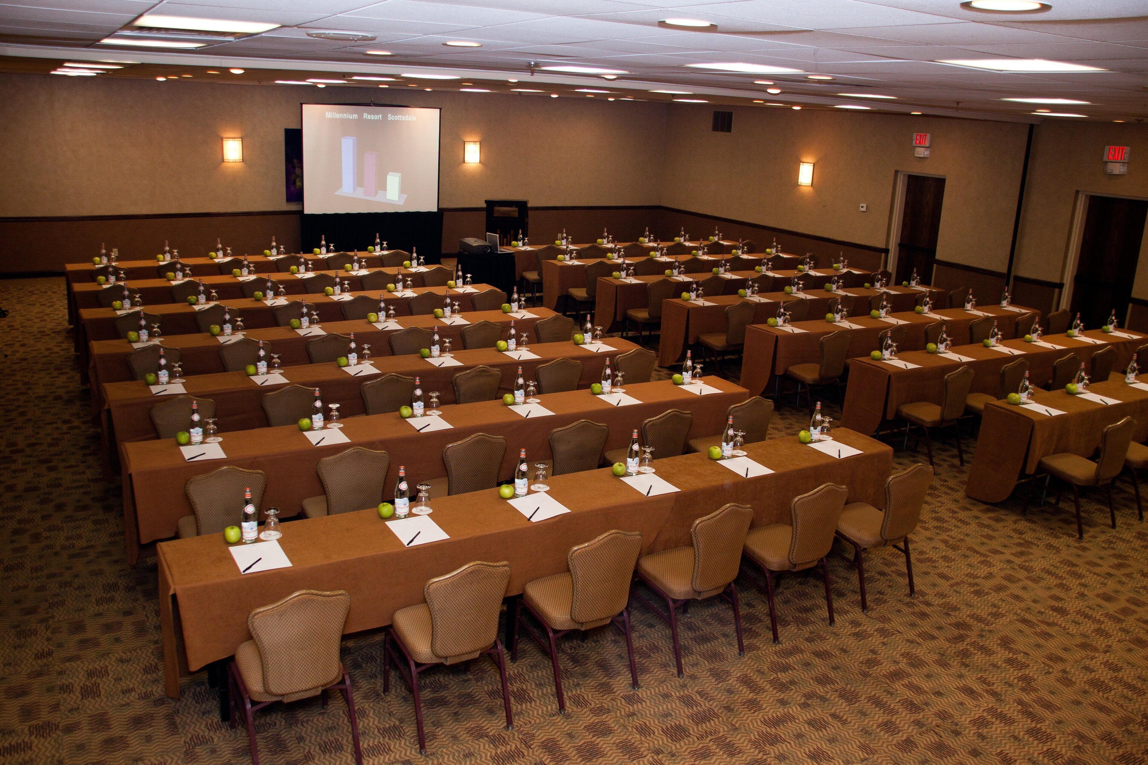 A conference room with rows of tables, chairs, and a projector screen.