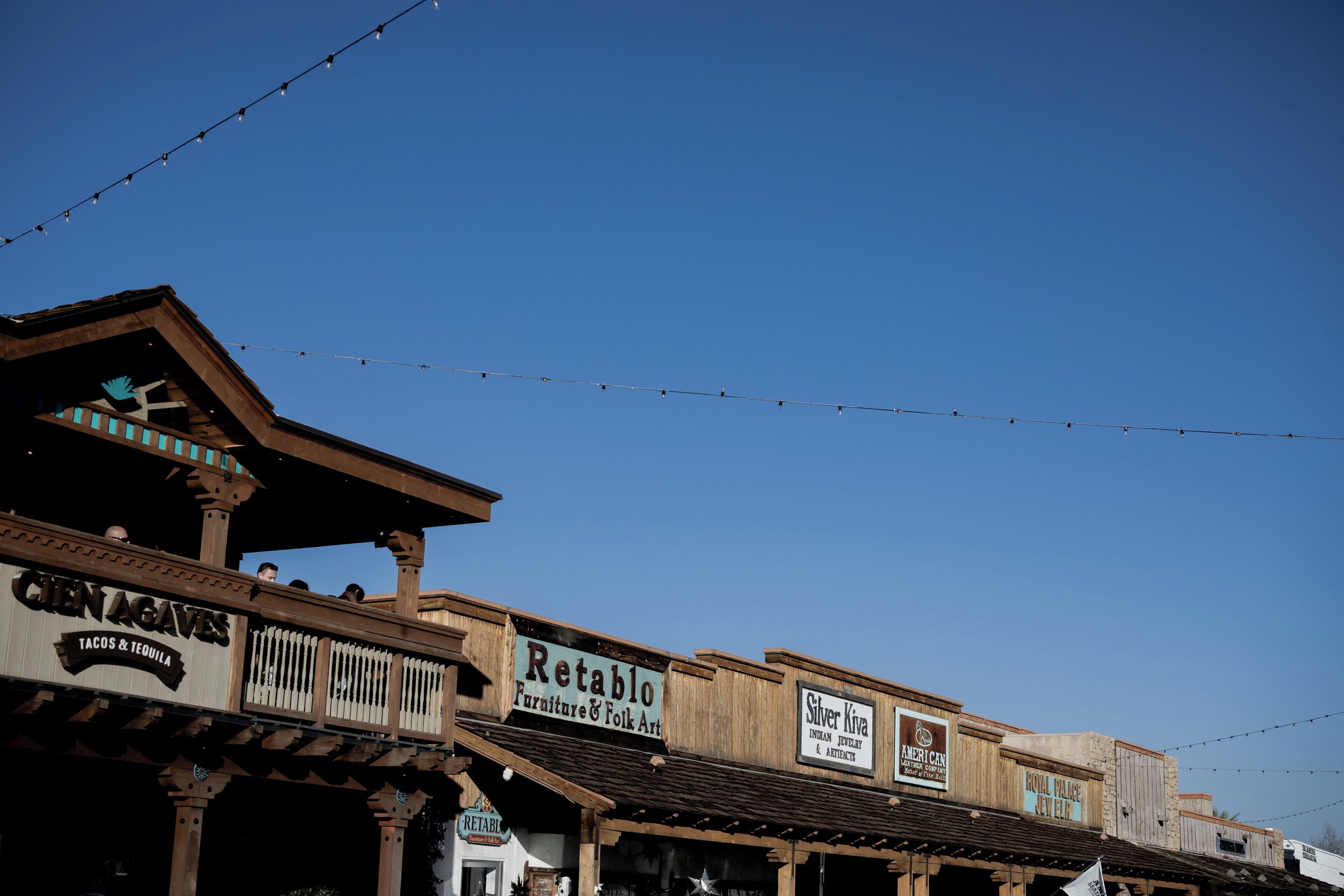 A row of wooden buildings with signs for businesses like 'Cien Aguas' and 'Retablo.'