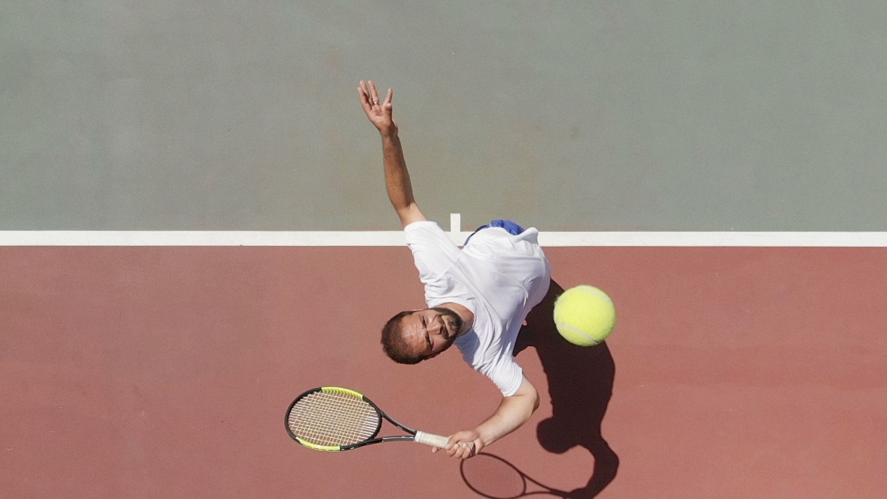 A tennis player in mid-action on a court with a racket and ball.