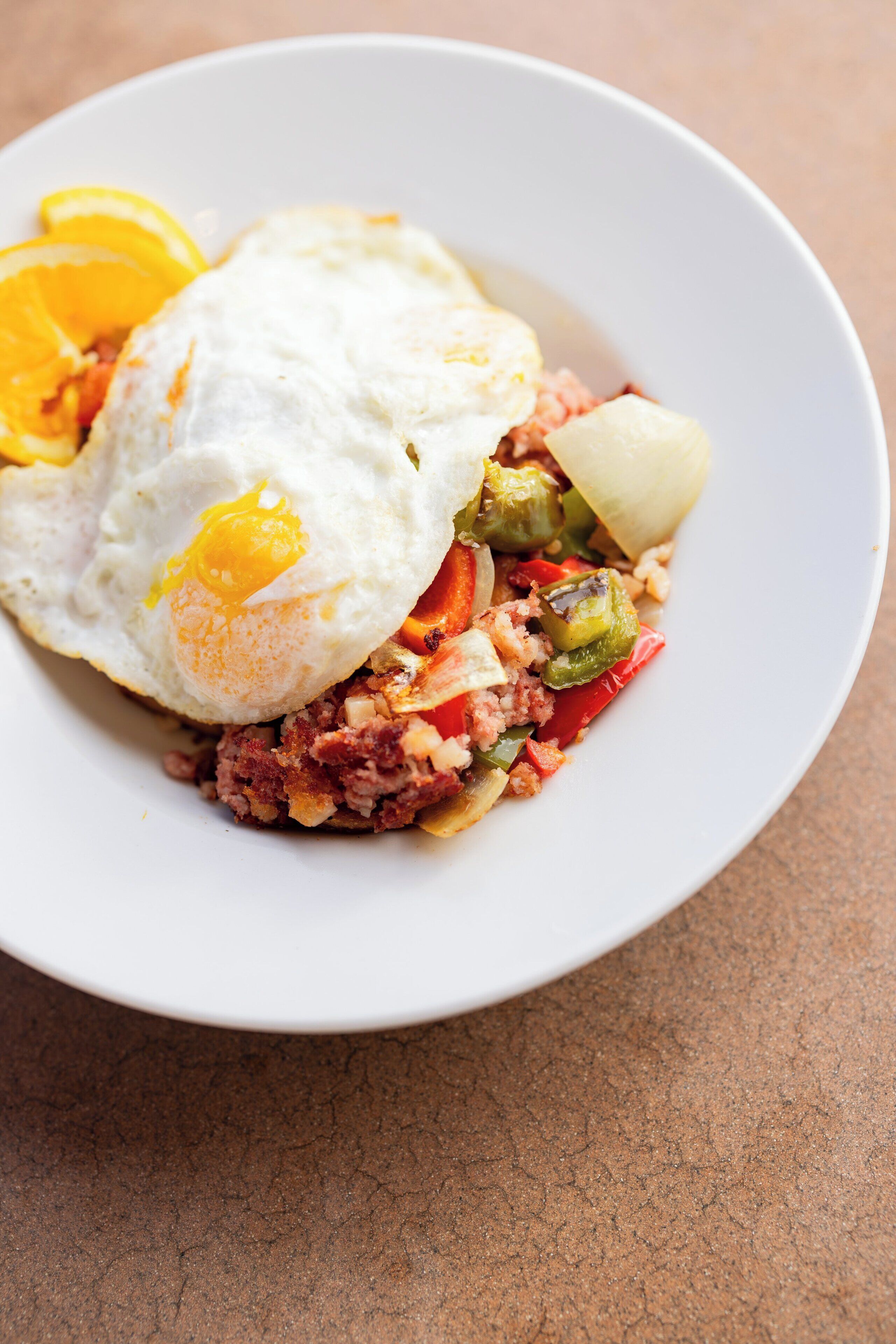 A white plate with a fried egg, vegetables, and a slice of orange.