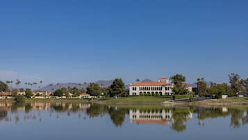 A large building with a red roof, a reflection in the water, and palm trees in the background.