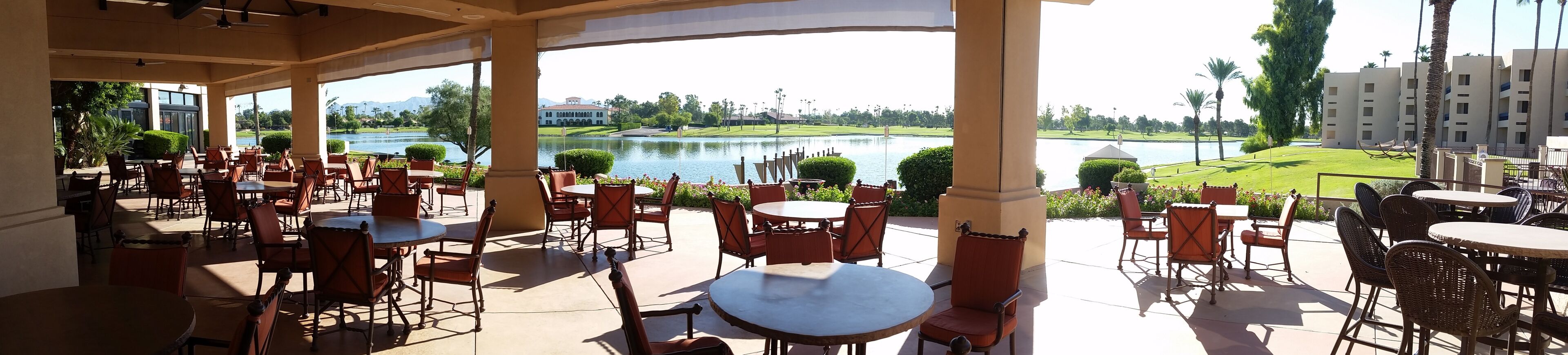 Un espacio al aire libre con mesas y sillas, con vistas a un lago y un campo de golf.