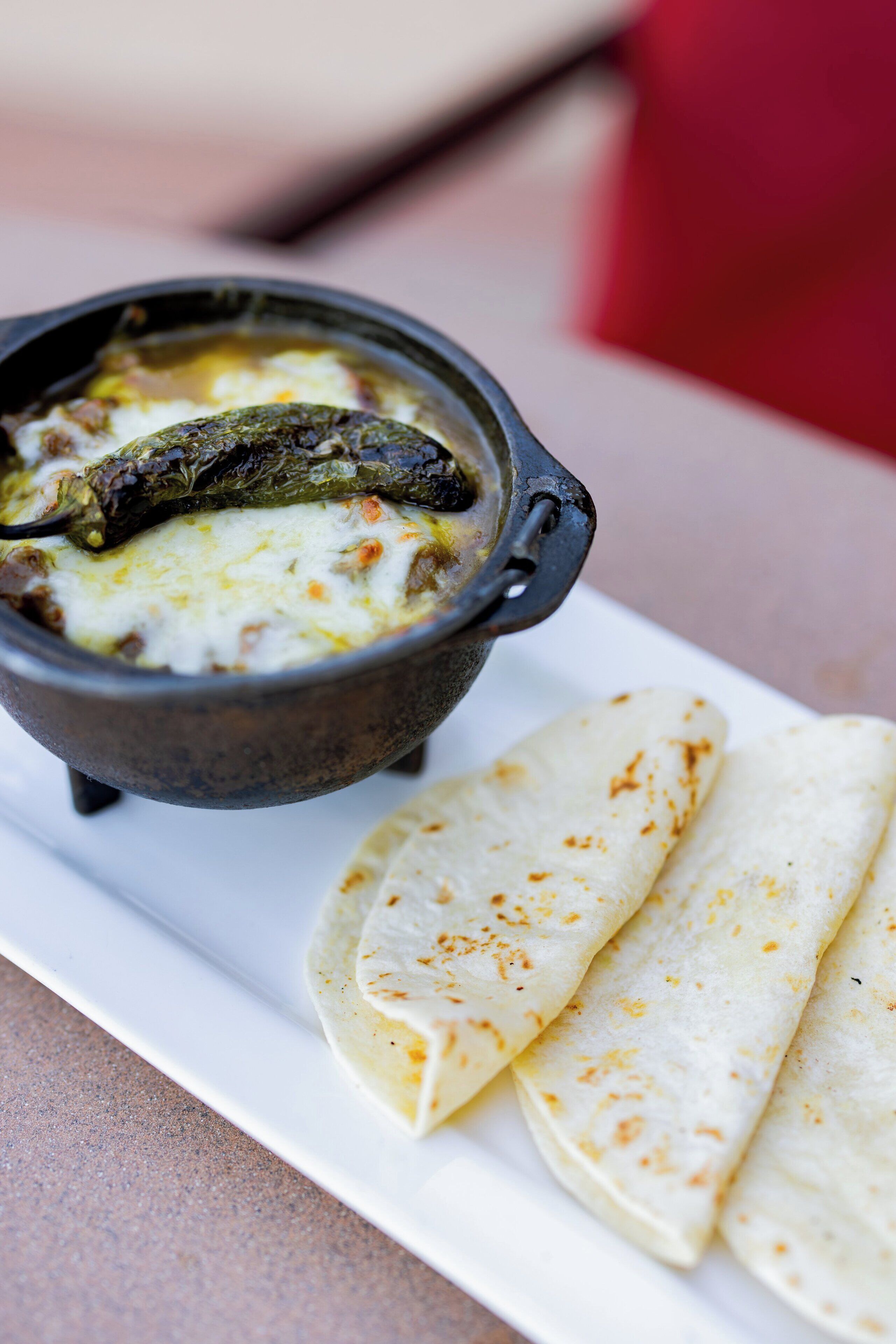 A white plate with a black bowl containing a soup and flatbread.