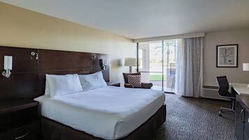 A hotel room with a large bed, a desk, a chair, a lamp, and a view of the outdoors.