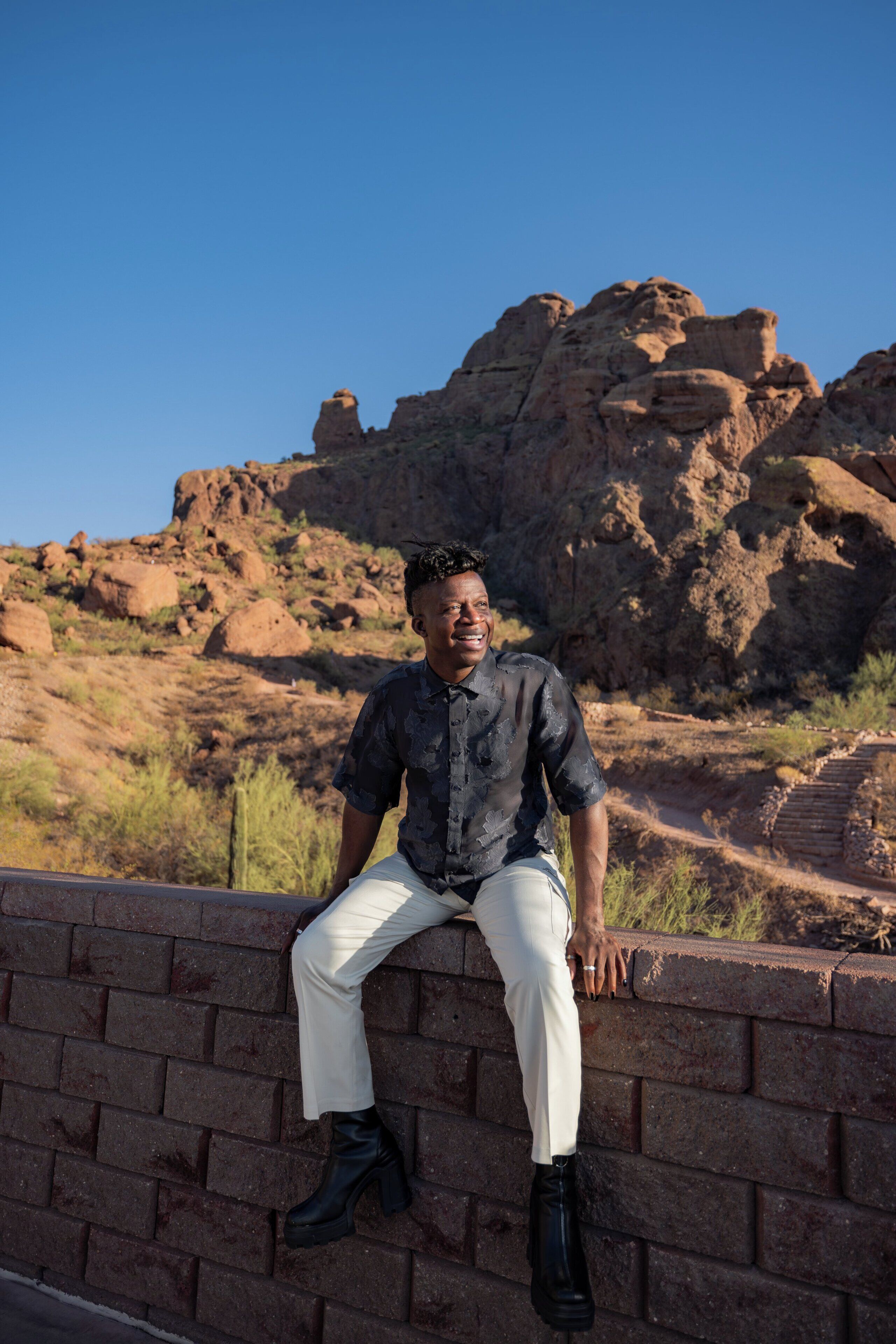 A person sitting on a brick wall with a rocky landscape in the background.