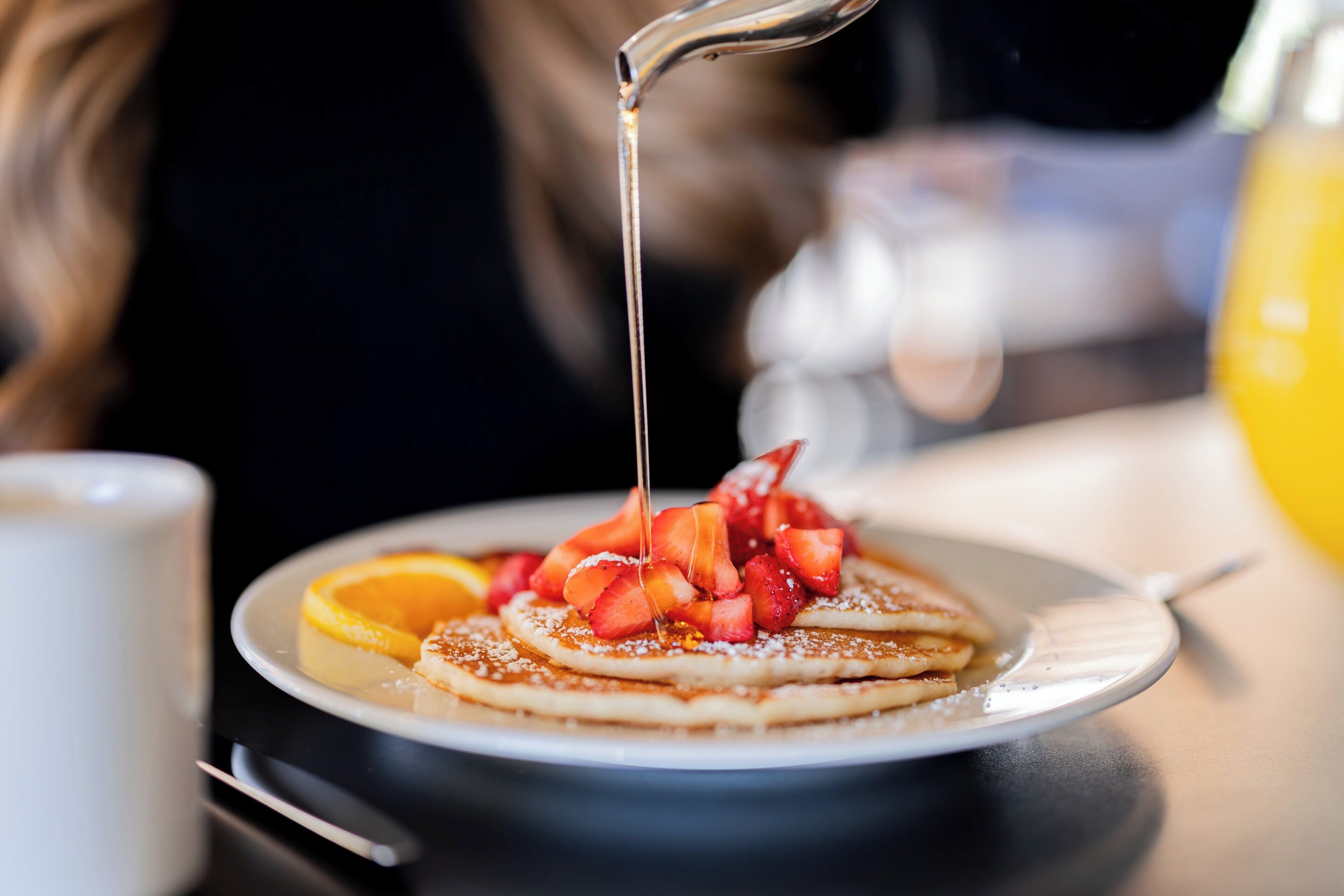 Une assiette de crêpes garnies de fraises et nappées de sirop, une tasse et un récipient jaune.