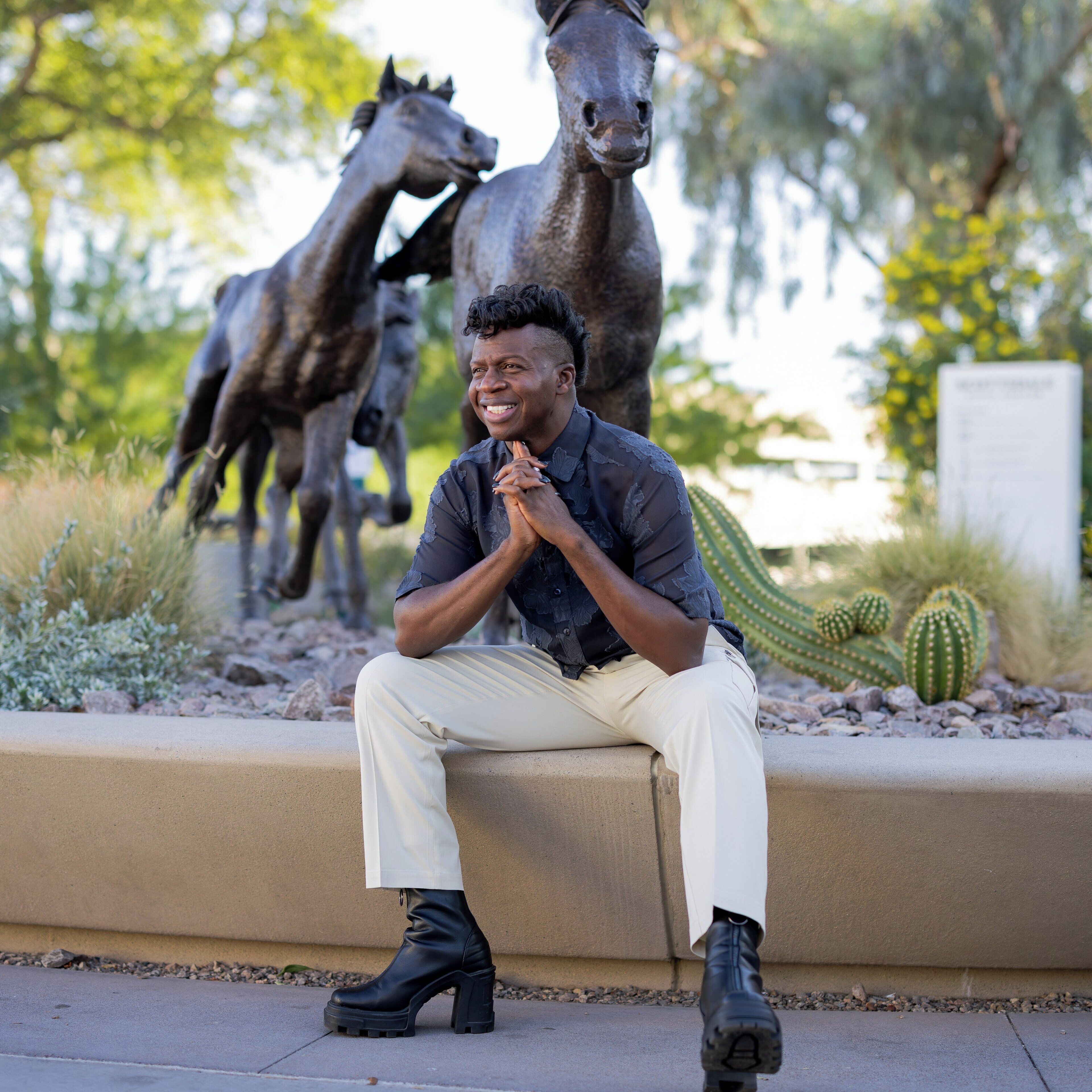 A person sitting on a concrete ledge with a sculpture of horses behind them.