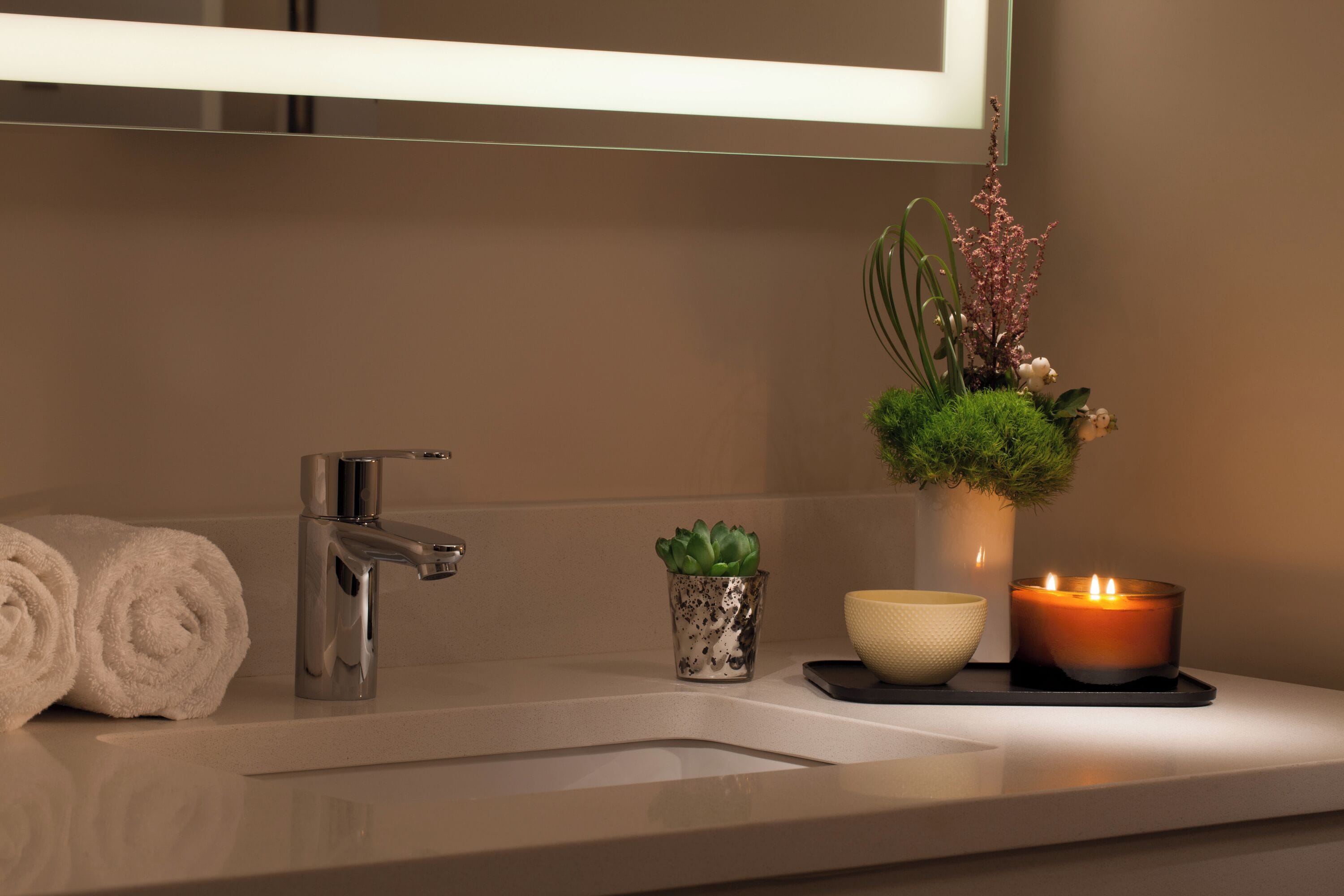 Un bagno con un lavandino moderno, uno specchio, un asciugamano, una piccola pianta in vaso, una candela e una ciotola.