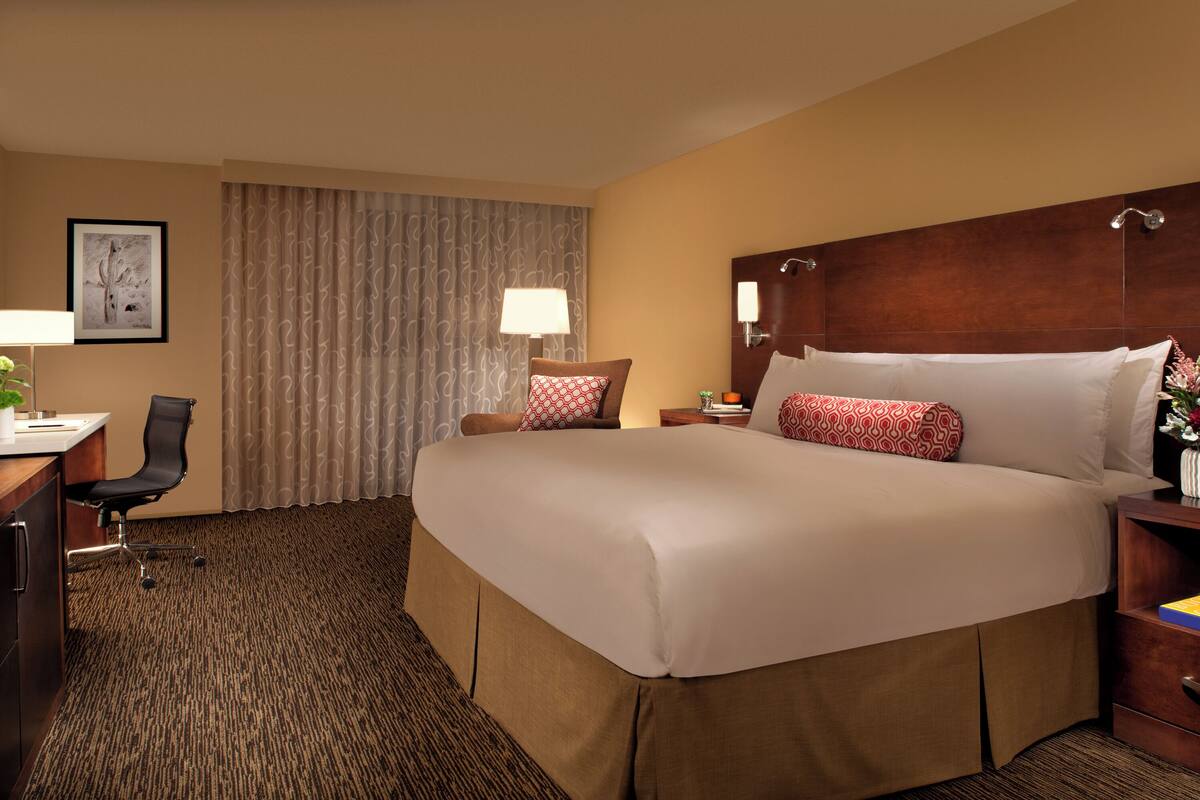 A hotel room with a large bed, a desk, a chair, and a window with curtains.