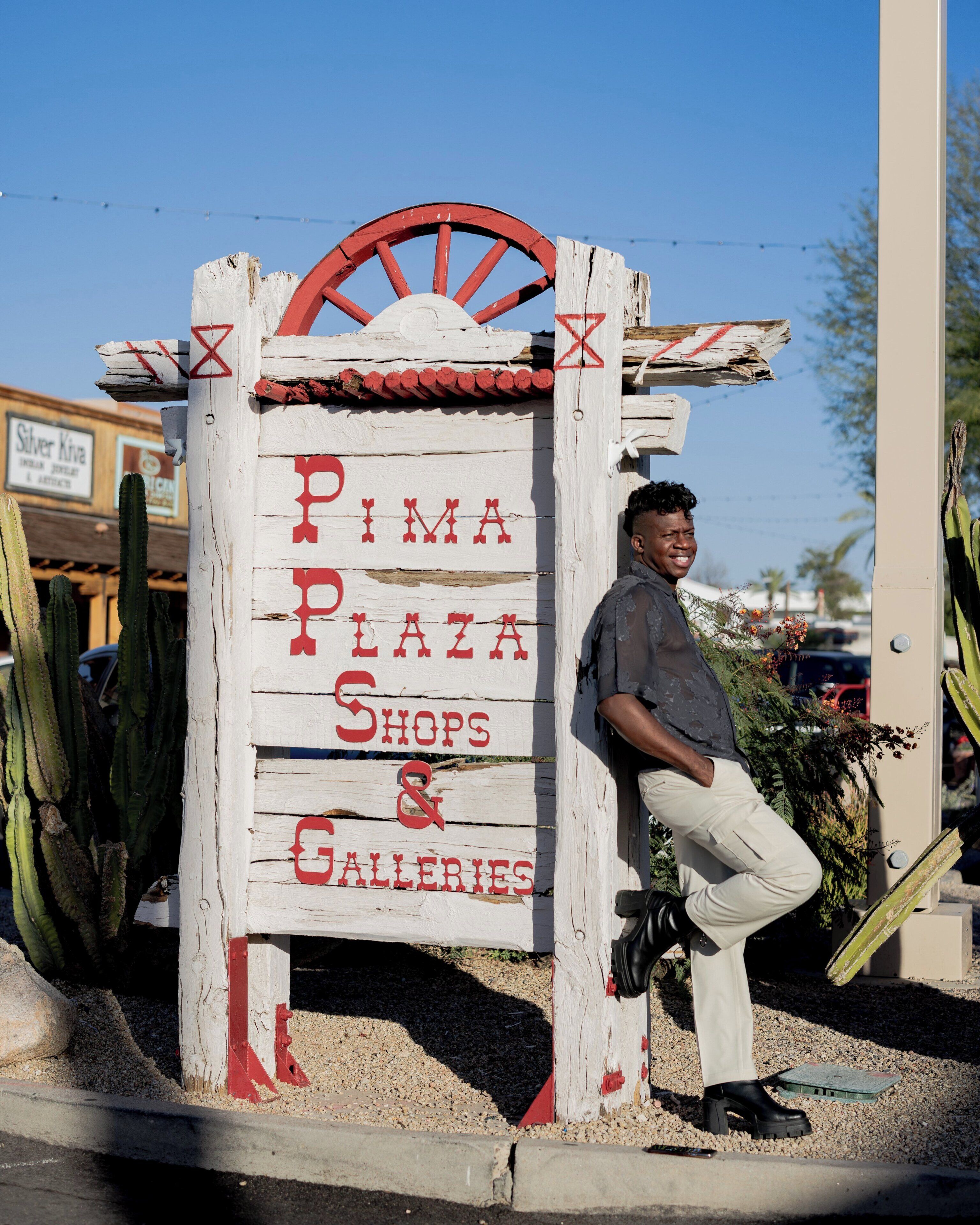 Ein hölzernes Schild mit dem Text 'Pima Plaza Shops & Galleries' und einem roten Rad.