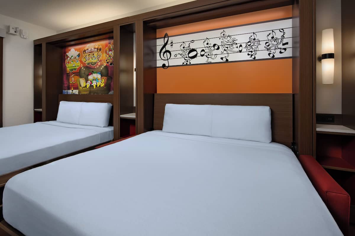Two single beds with white linens, a wooden headboard, a wall with a musical note design, and a red bench.