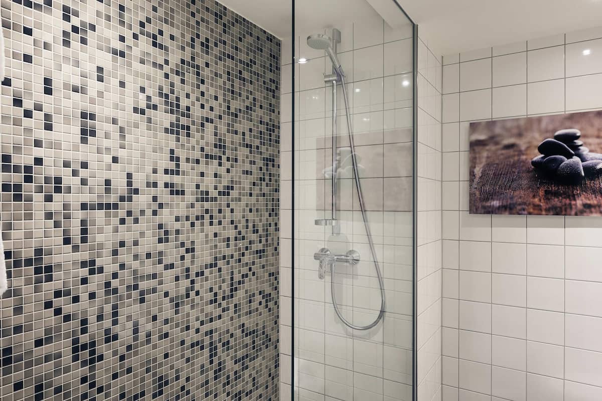 Et moderne badeværelse med en væg i mosaikfliser, en glas brusekabine og et billede i ramme.