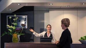 Modernilla designilla varustettu vastaanottotiski, maljakko täynnä kukkia ja televisioruutu.