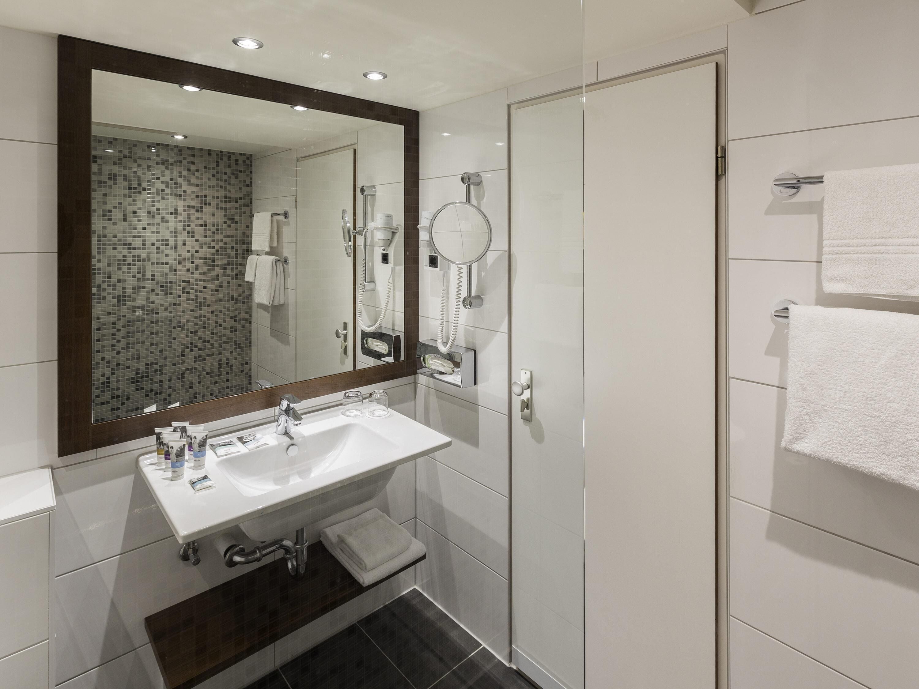 Un bagno moderno con un ampio specchio, un lavandino, una doccia e un portascopevoli.