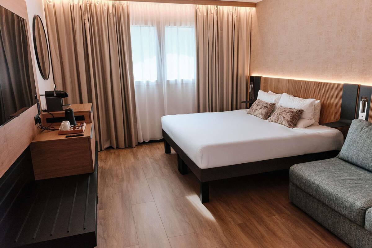 A hotel room with a bed, a desk, a chair, and a sofa.