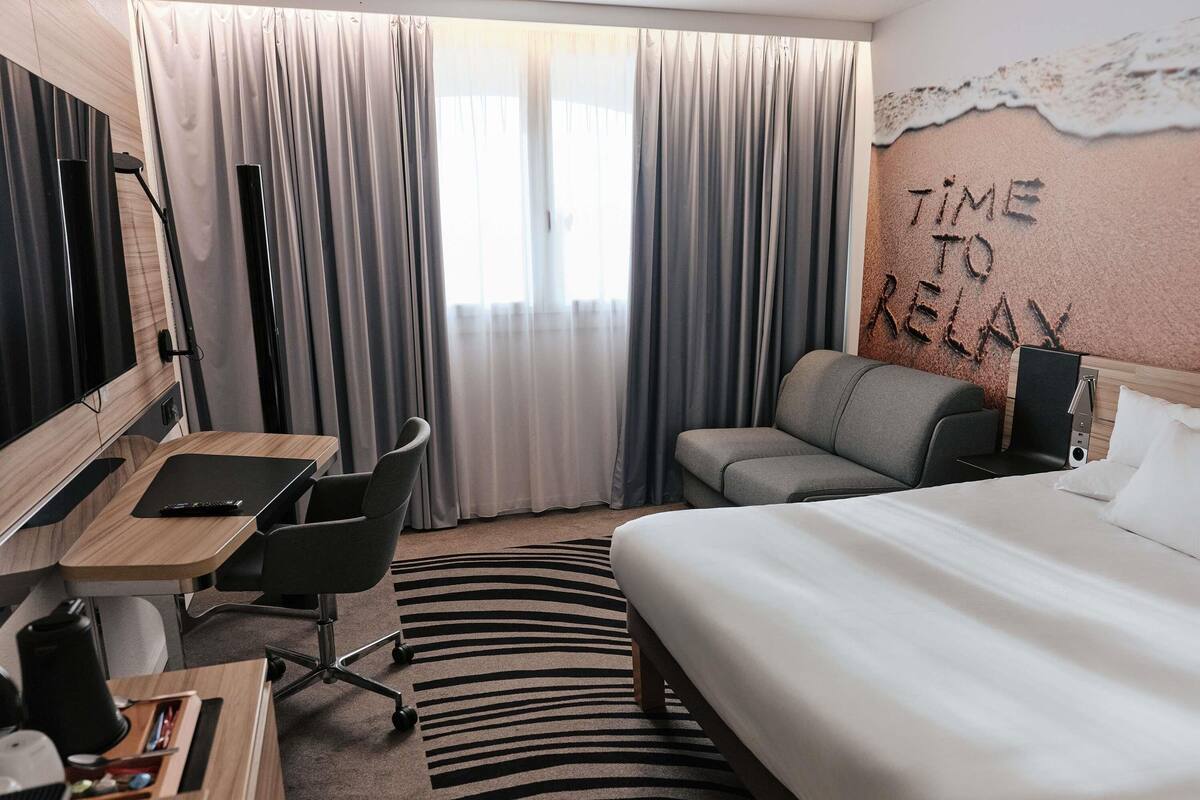 A hotel room with a bed, a desk with a chair, a sofa, and a TV.