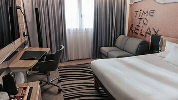 A hotel room with a bed, a desk with a chair, a sofa, and a TV.