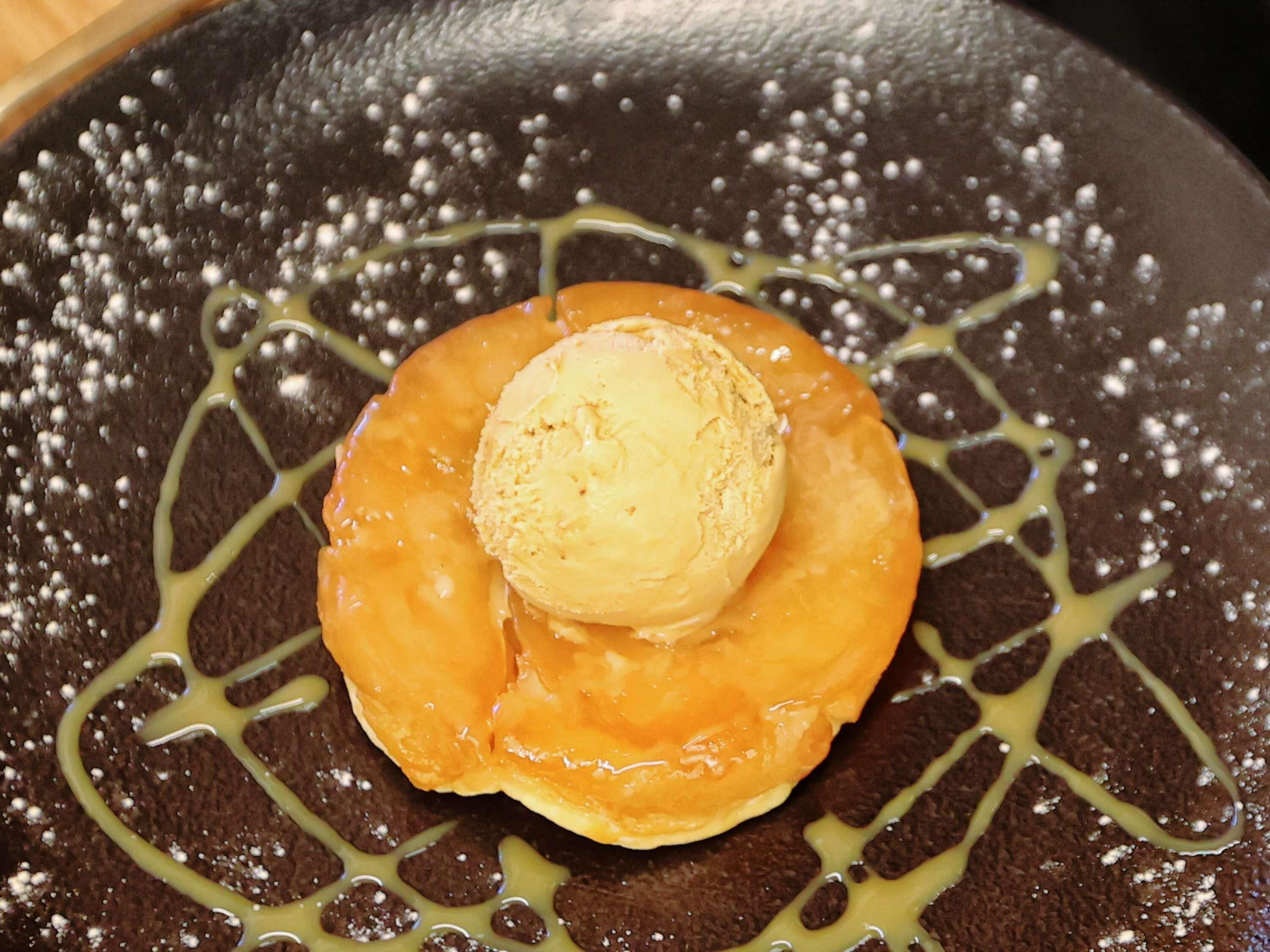 Ein Dessert mit einer Kugel Eis, umgeben von einem karamellisierten Gebäck, serviert auf einem Teller mit dunklem Hintergrund und Karamellsauce.