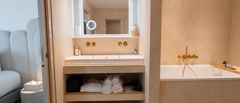 A modern bathroom with a large mirror, a bathtub, and a vanity with a sink and storage.