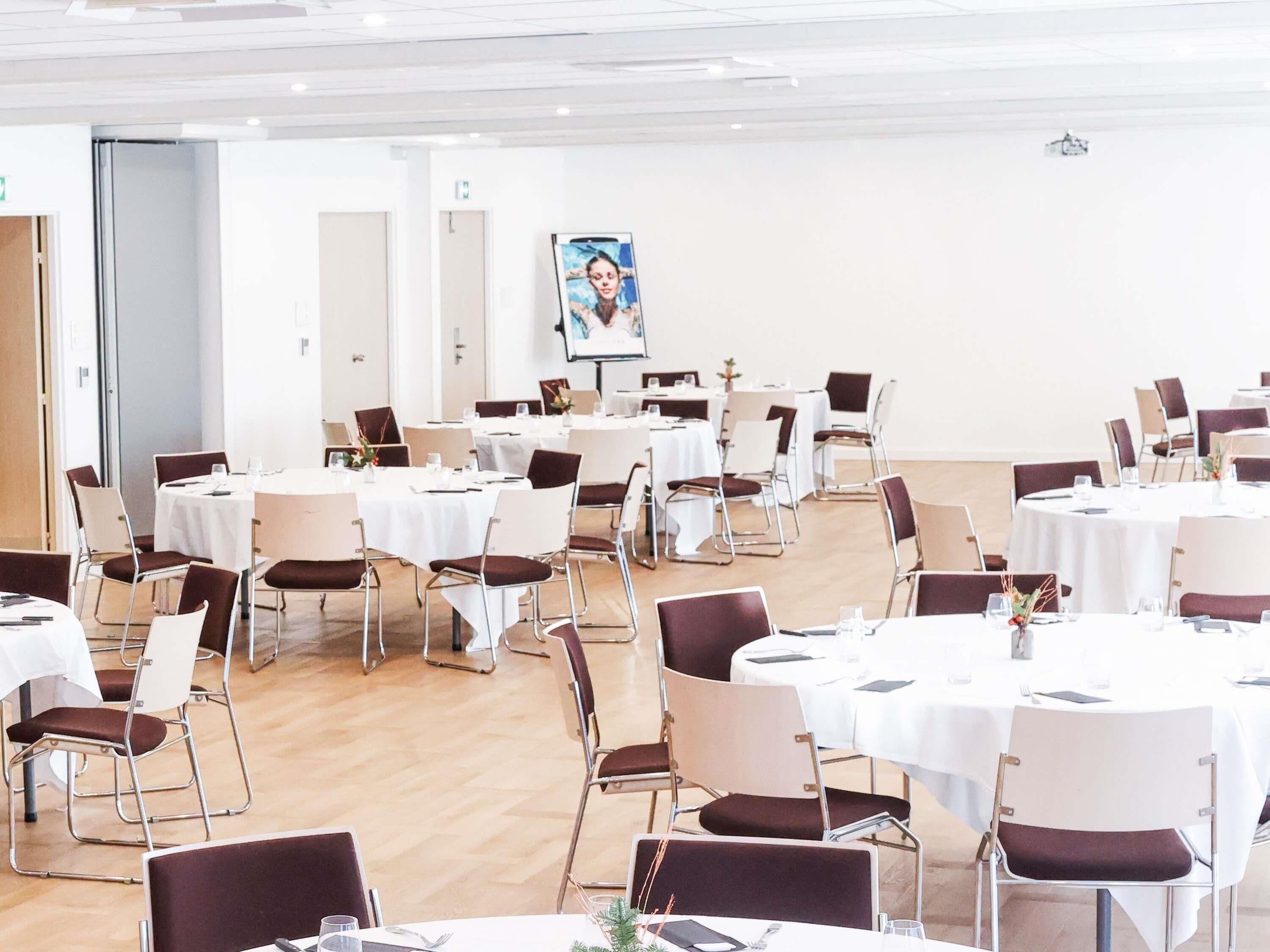 Ein Konferenzraum mit runden Tischen, Stühlen und einem großen Plakat an der Wand.