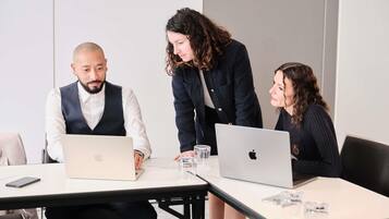Drie personen in een vergaderruimte met laptops en glazen water op tafel.