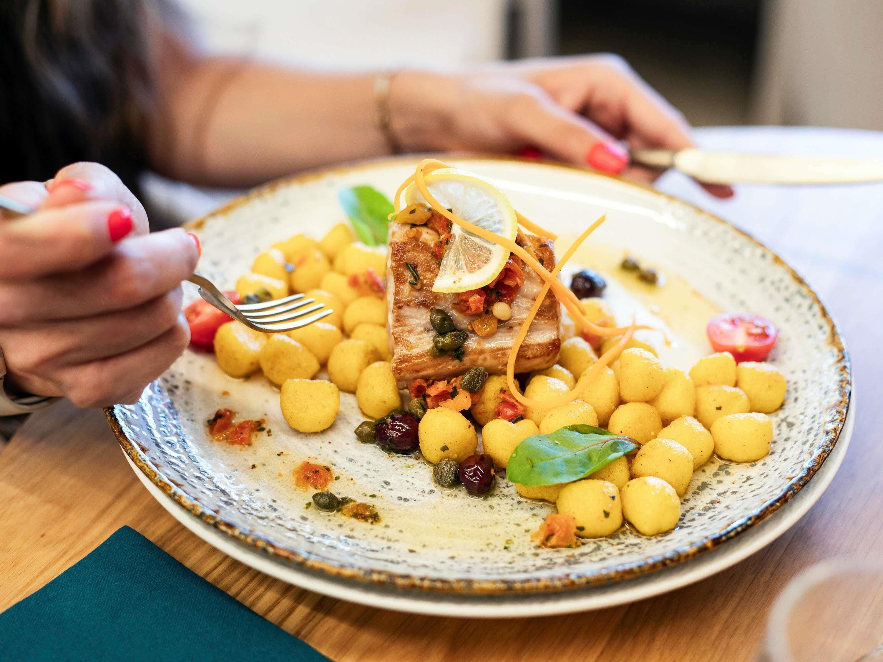 Ein Teller mit Fischfilet, Zitrone, Kapern und dazu gelbe Pasta.