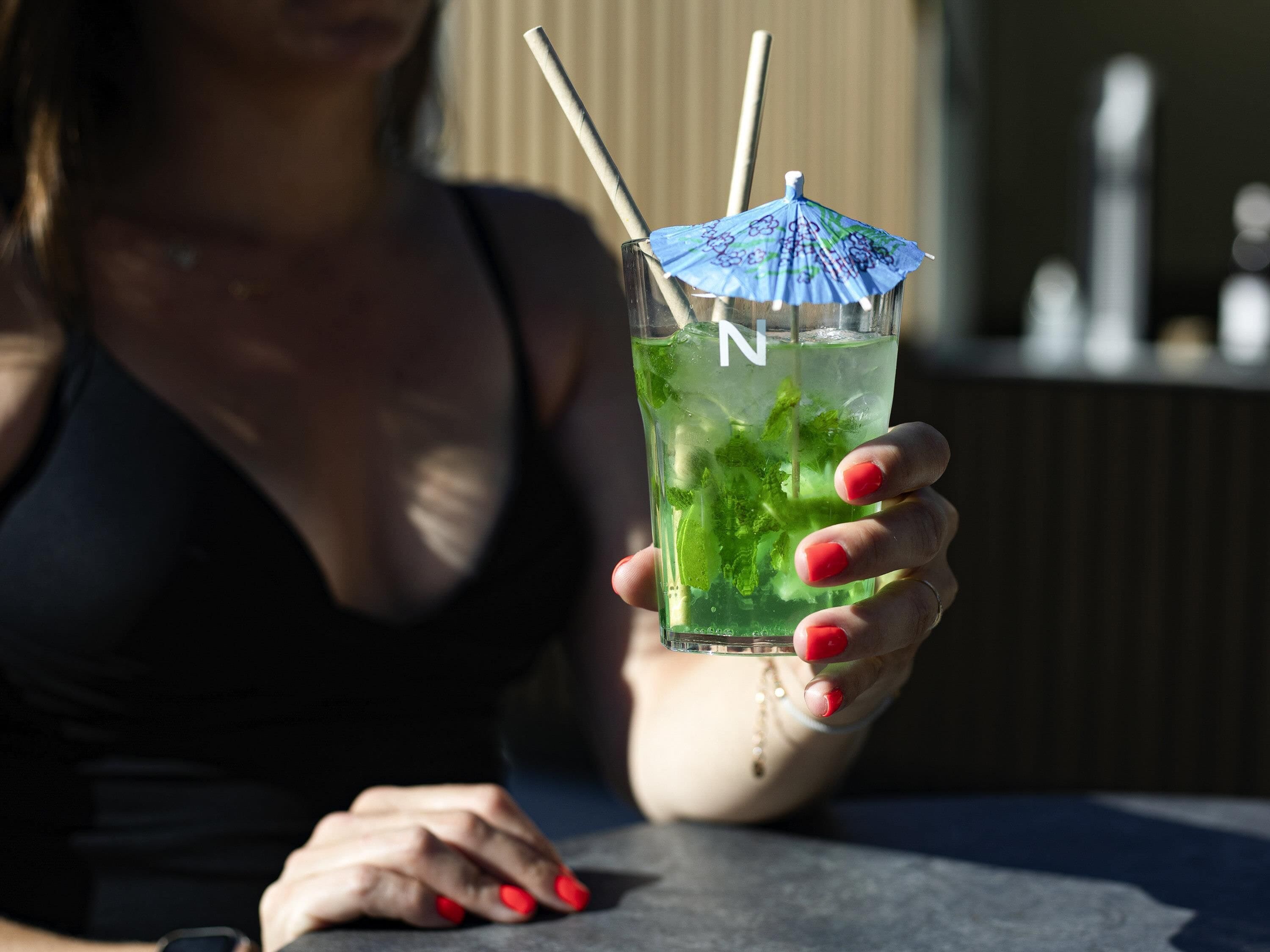 A person holding a glass with a straw and a blue umbrella decoration, containing a green drink with mint leaves.