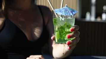 A person holding a glass with a straw and a blue umbrella decoration, containing a green drink with mint leaves.