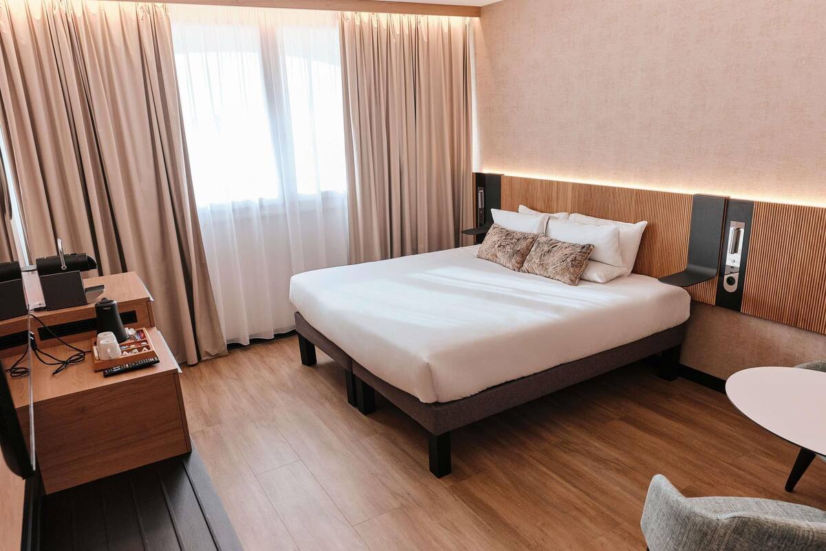 A hotel room with a large bed, a desk with a laptop, a chair, and a small table.