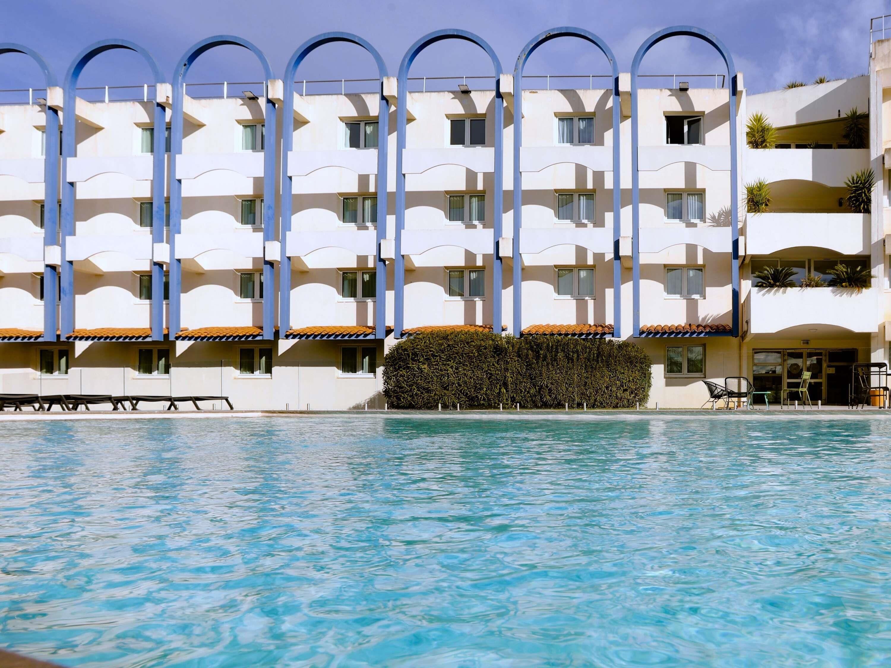 Ein Hotel mit Pool, mehreren Balkonen und blauem Himmel.