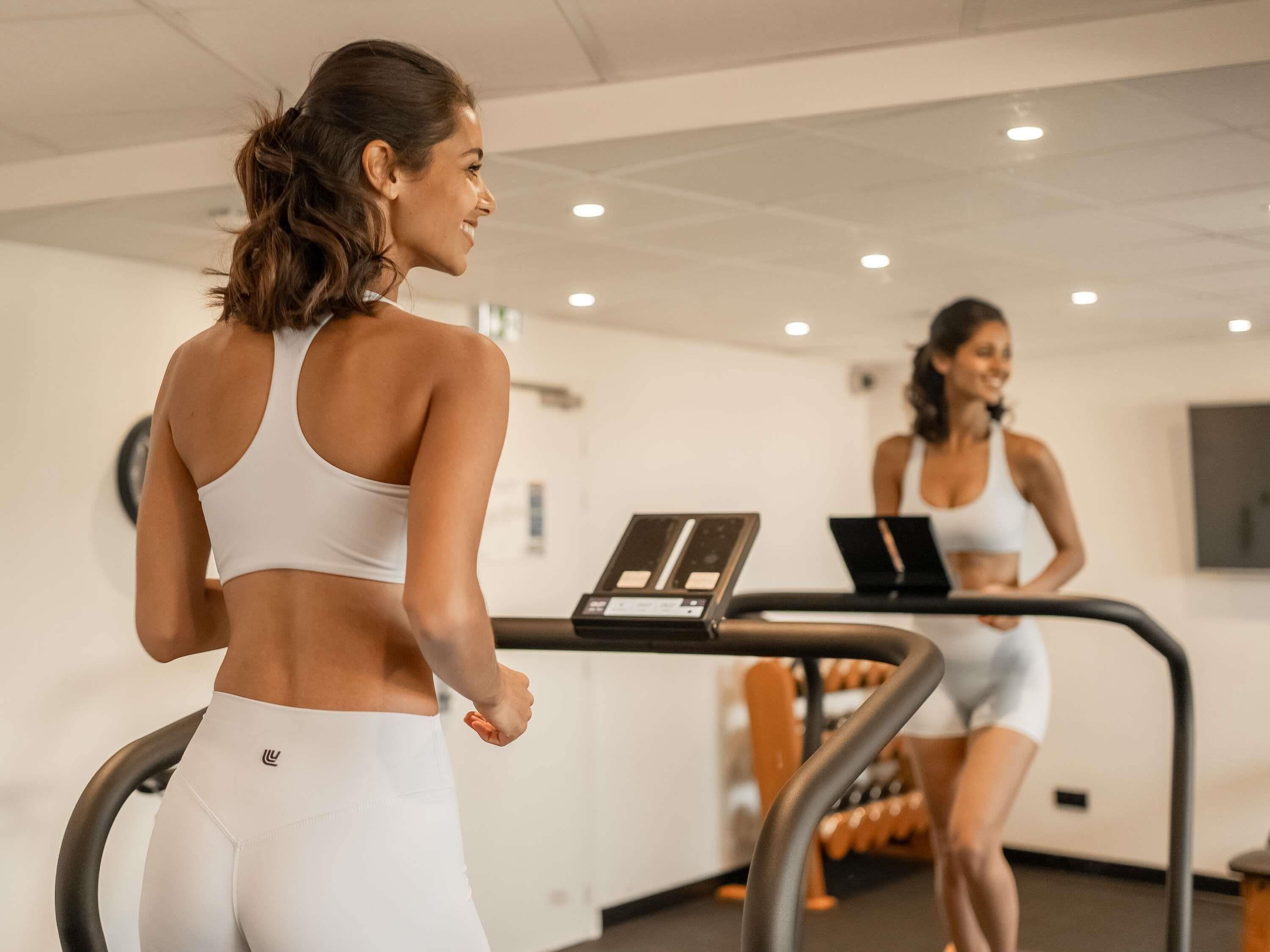 Una palestra con tapis roulant, uno specchio a parete e un portatile su una delle macchine.