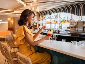 En person som sitter vid en bardisk med ett glas i handen, barstolar och en bardisk.