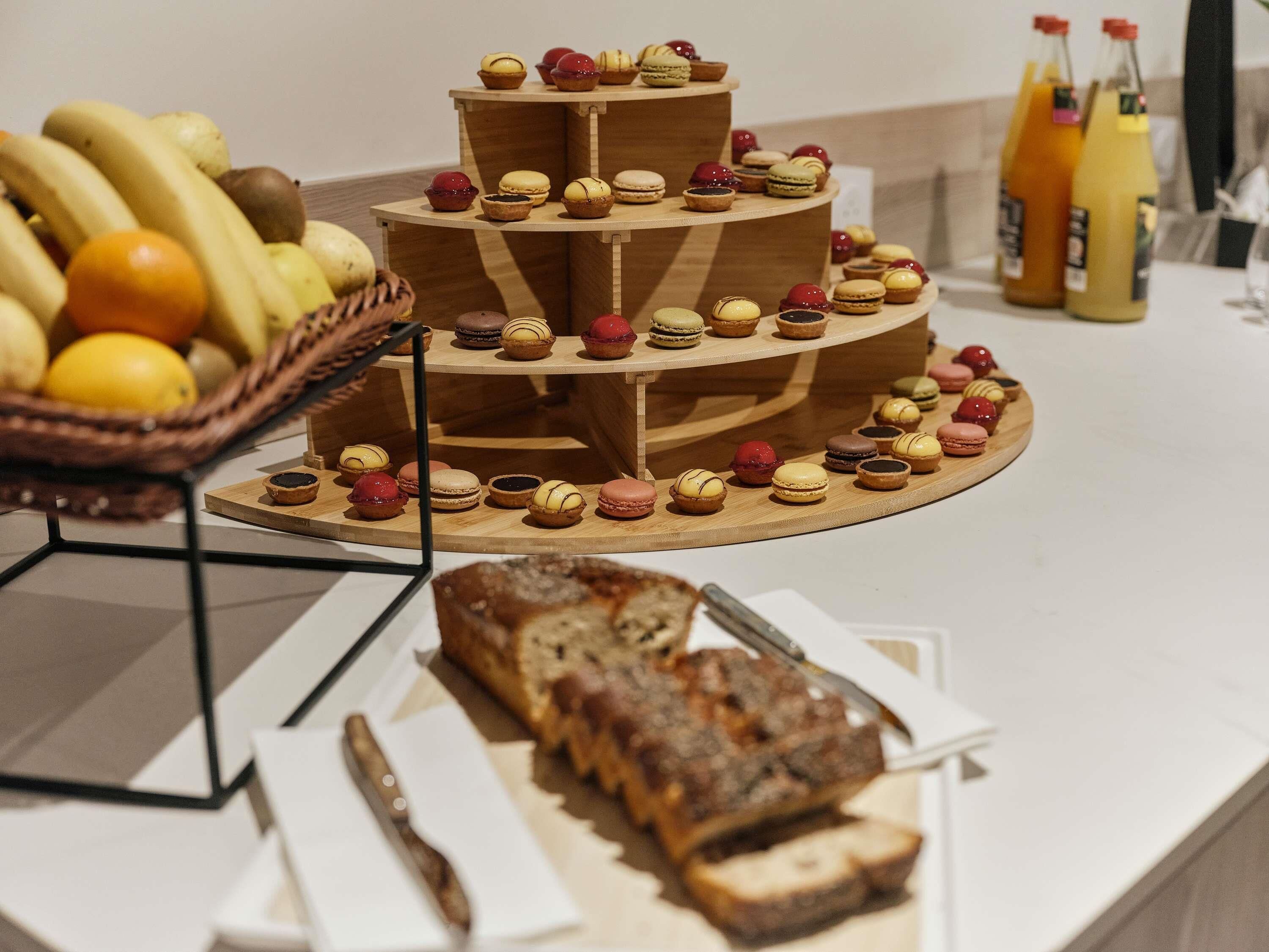 A three-tiered wooden stand with assorted pastries and a loaf of bread on a table.