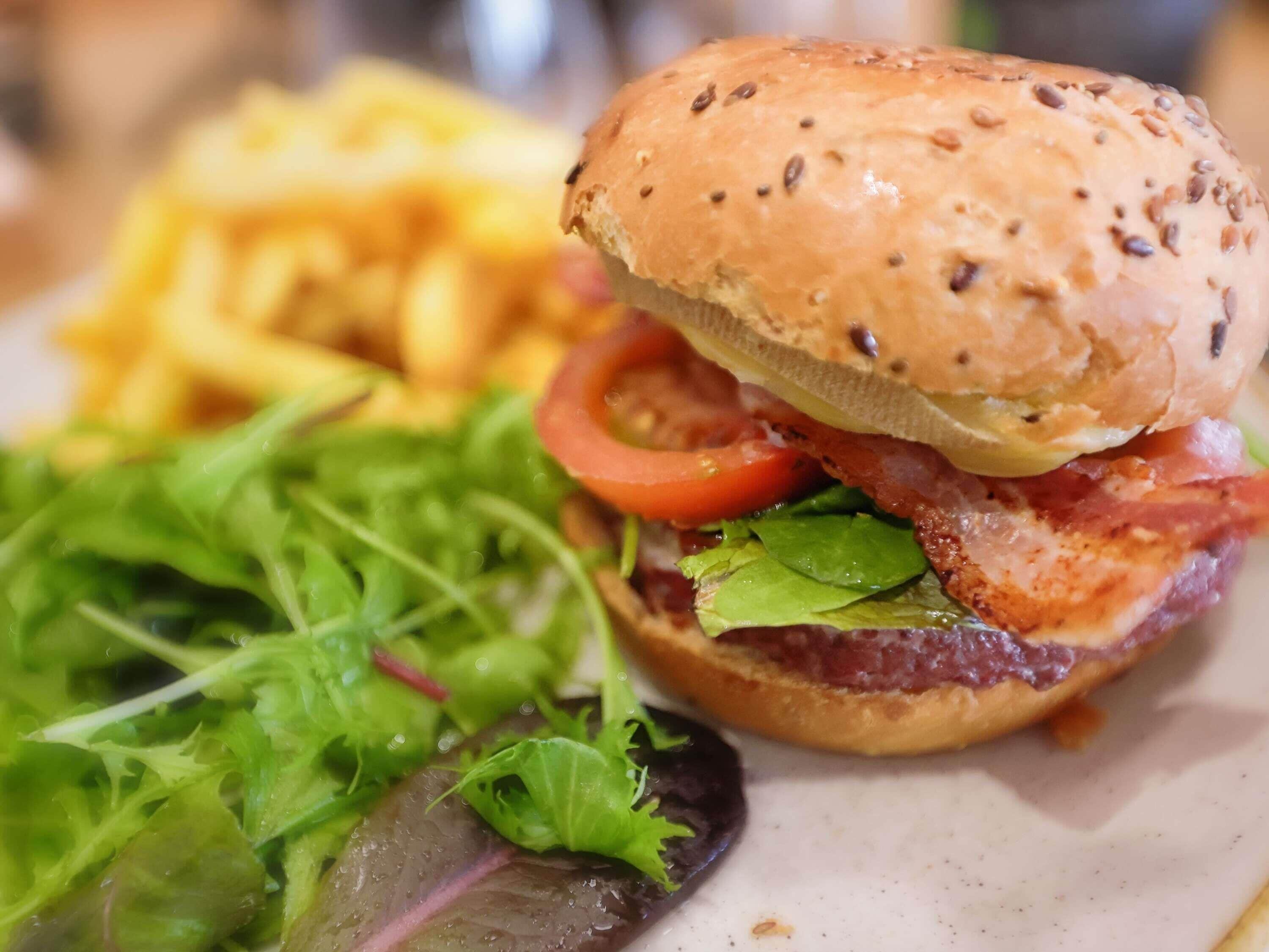A burger with lettuce, tomato, and bacon, alongside a side of fries and a salad.