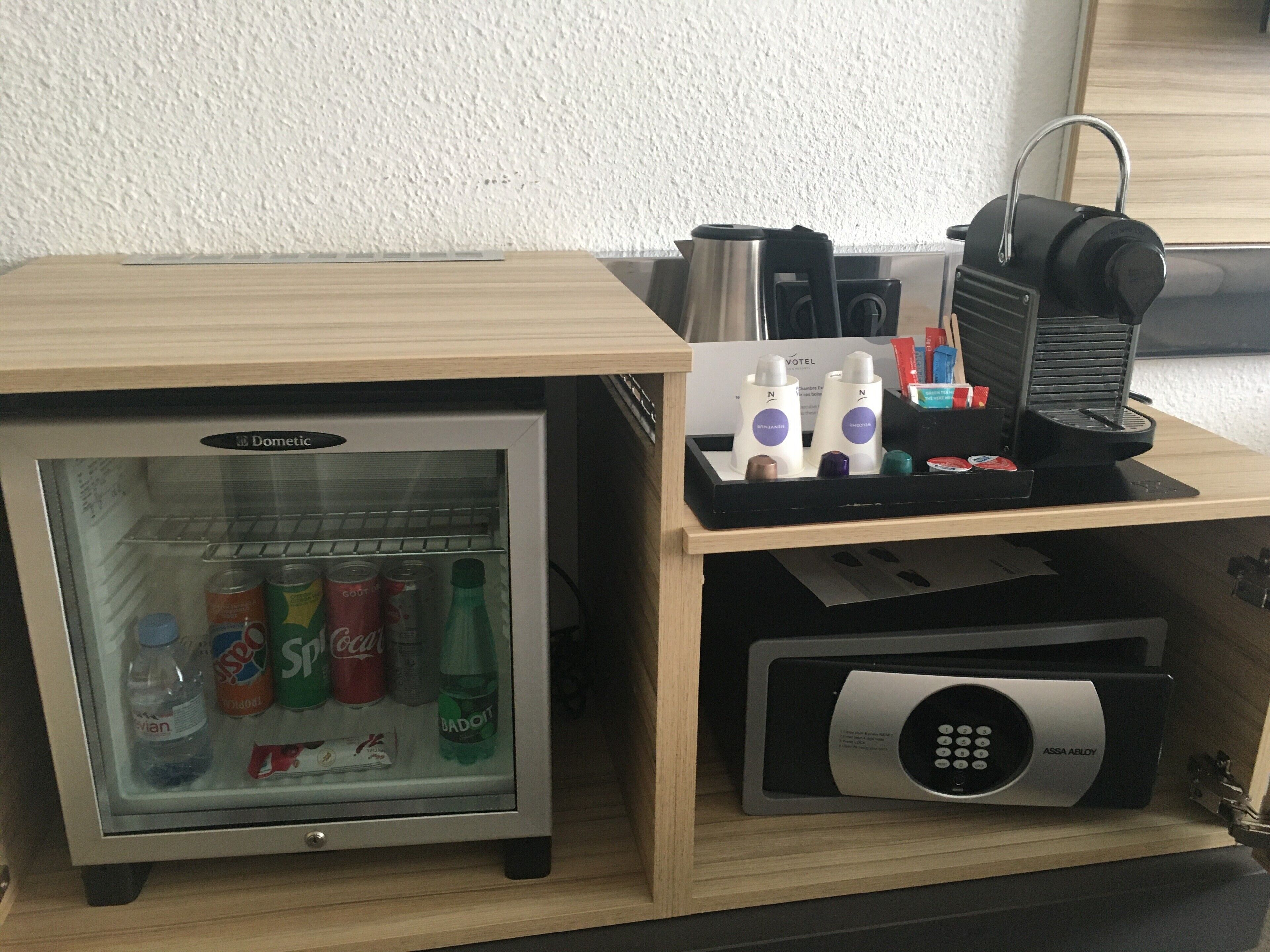 A minibar with a refrigerator containing beverages, a coffee machine, and a bottle of water.