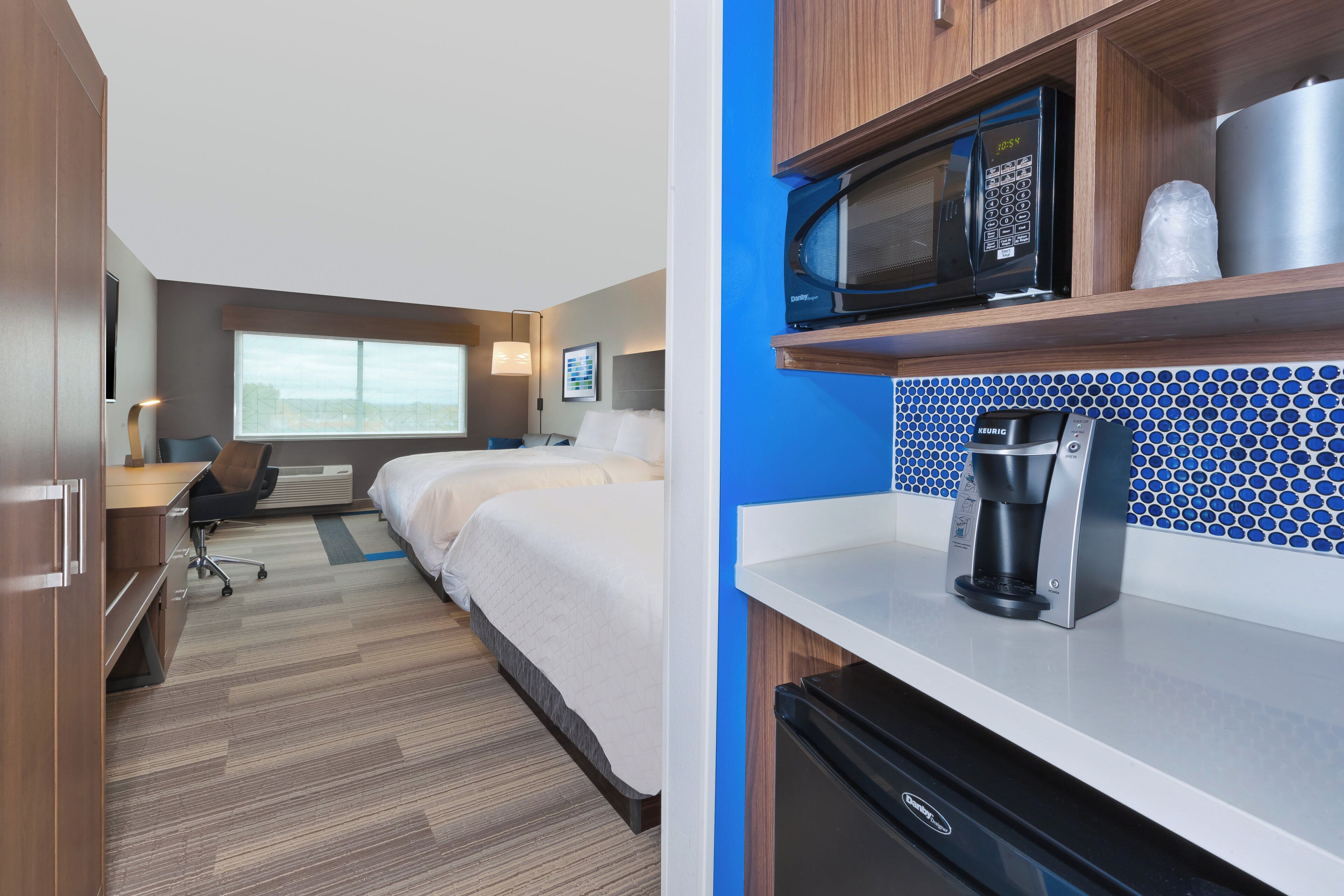 A hotel room with a kitchenette, a bed, a desk, and a window.